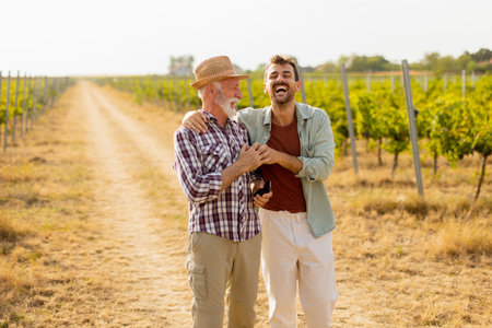 Walking along a dusty path in a sunny vineyard, two men engage in lighthearted conversation, their camaraderie evident against the backdrop of sprawling grapevinesの写真素材