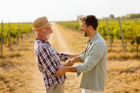 Two men share a meaningful discussion amidst rows of grapevines, enjoying the warmth of the late afternoon sun, symbolizing connection and tradition in viticultureの写真素材