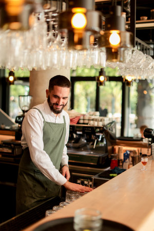 With a warm smile, the bartender skillfully crafts cocktails in a lively bar, where sunlight floods through large windows, creating a vibrant atmosphereの写真素材