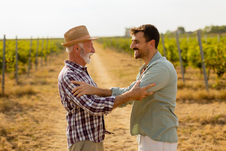 Two men share a meaningful discussion amidst rows of grapevines, enjoying the warmth of the late afternoon sun, symbolizing connection and tradition in viticultureの写真素材