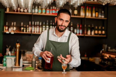 In a lively bar setting, a confident bartender mixes a fresh cocktail, showcasing his expertise with a bottle in hand, ready for the night's rushの写真素材