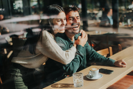 Young couple shares tender moments at a cafÃ©, surrounded by greenery and natural light, as they connect over warm drinks and playful gesturesの写真素材
