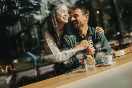 Young couple shares tender moments at a cafÃ©, surrounded by greenery and natural light, as they connect over warm drinks and playful gesturesの写真素材