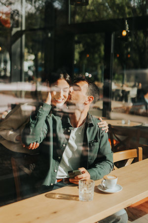 Young couple shares tender moments at a cafÃ©, surrounded by greenery and natural light, as they connect over warm drinks and playful gesturesの写真素材