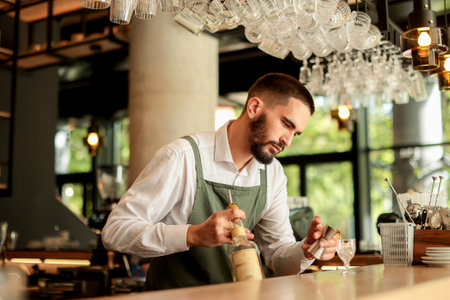 Bartender concentrates as he skillfully crafts a cocktail, surrounded by an array of glassware in a...