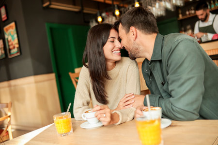 Couple shares a joyful moment at a stylish cafÃ©, sipping coffee and enjoying bright orange juice while laughing together, surrounded by a welcoming atmosphereの写真素材
