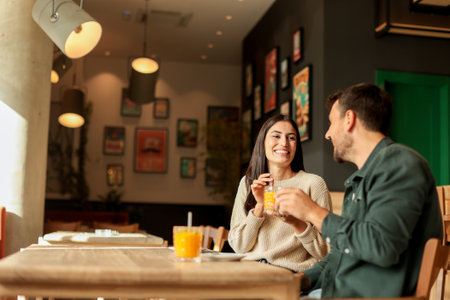 Couple shares a joyful moment at a stylish cafÃ©, sipping coffee and enjoying bright orange juice while laughing together, surrounded by a welcoming atmosphereの写真素材