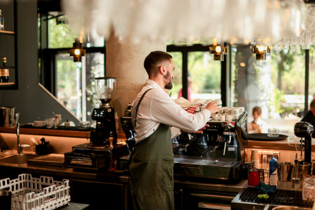 Dedicated barista expertly prepares espresso while engaging with a lively atmosphere filled with sunlight, plants, and happy customers savoring their drinksの写真素材