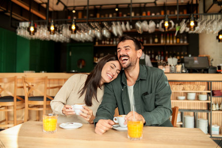 Couple shares a joyful moment at a stylish cafÃ©, sipping coffee and enjoying bright orange juice while laughing together, surrounded by a welcoming atmosphereの写真素材