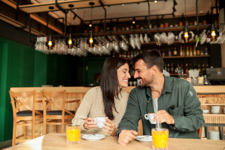 Couple shares a joyful moment at a stylish cafÃ©, sipping coffee and enjoying bright orange juice while laughing together, surrounded by a welcoming atmosphereの写真素材