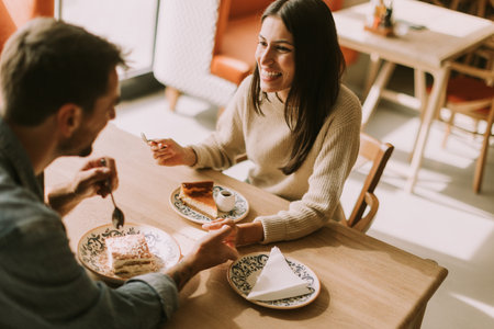 In a warm, inviting cafe, a couple shares laughter and delightful treats, savoring coffee and pastries while basking in the afternoon sun.の写真素材