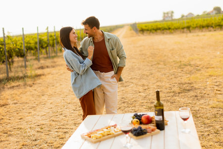Basking in the warm sunlight, a joyful couple embraces as they revel in a delightful picnic among the grapevines, savoring wine and gourmet treatsの写真素材