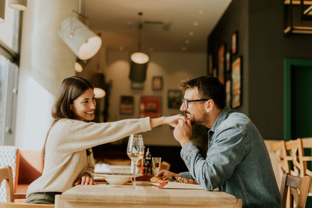 A couple dines in a trendy eatery, playfully sharing food while immersed in conversation. The warm ambiance complements their joyful connection, creating a memorable moment.の写真素材