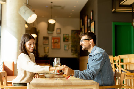 A couple enjoys a delightful evening, sharing dishes of flavorful cuisine and laughter while seated at a wooden table in a relaxed restaurant atmosphere.の写真素材
