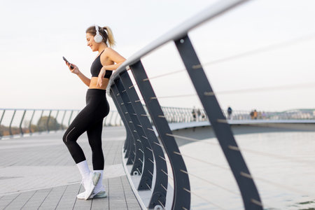 Outside a contemporary building, a woman relishes her workout, immersed in music through headphones while enjoying the sunny atmosphere of the city parkの写真素材