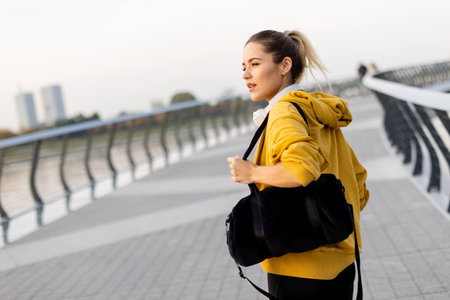 Walking along the riverside path, a cheerful woman in a yellow hoodie beams with joy. The evening sky casts a warm glow, creating a serene atmosphere for a leisurely strollの写真素材