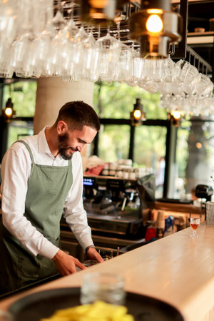 With a warm smile, the bartender skillfully crafts cocktails in a lively bar, where sunlight floods through large windows, creating a vibrant atmosphereの写真素材
