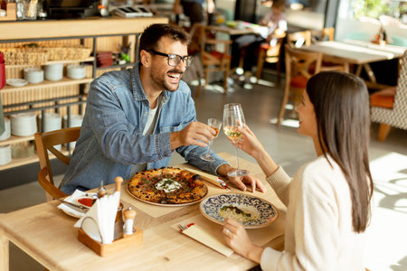 Two individuals savor their drinks at a wooden table, immersed in a relaxed restaurant vibe, while deep in conversation and laughter.の写真素材