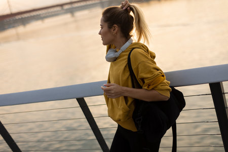 A carefree woman walks along a contemporary riverside path, her cheerful demeanor captured as she enjoys the picturesque sunset and fresh air.の写真素材