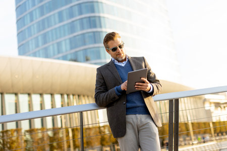 An elegant individual in a blazer stands on a balcony at sunset, holding a tablet and gazing over a vibrant metropolis, embodying professionalism and relaxation.の写真素材