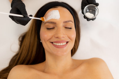 A patient enjoys a skin treatment as a skilled professional applies a soothing mask, surrounded by calming decor, in a tranquil wellness center atmosphere.の写真素材