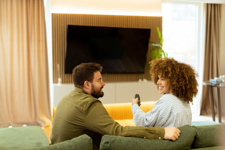 Seated on a comfortable couch, a couple shares a light-hearted moment, laughing and watching their favorite show while surrounded by a warm, inviting atmosphere.の写真素材