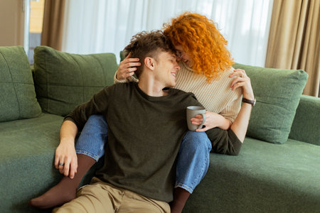 A couple enjoys a relaxing afternoon at home, seated comfortably on a plush sofa, exchanging loving smiles and laughter while sharing a warm beverage togetherの写真素材