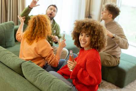 Four friends gather in a cozy living room, sharing laughter and drinks while seated on a comfy sofa. The atmosphere is warm and inviting, perfect for enjoying each other's company.の写真素材