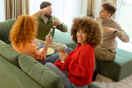 Four friends gather in a cozy living room, sharing laughter and drinks while seated on a comfy sofa. The atmosphere is warm and inviting, perfect for enjoying each other's company.の写真素材