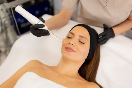 A therapist administers a high frequency therapy treatment, utilizing a glass electrode over a client's face. The process aims to refresh and revitalize the skin in a tranquil setting.の写真素材
