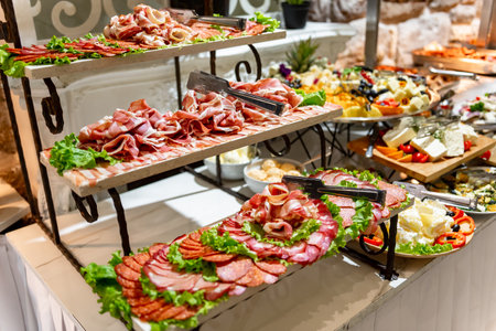 A vibrant display of various deli meats elegantly layered with fresh greens captivates the eye at a lively banquet. The setting is filled with guests enjoying gourmet offerings.の写真素材