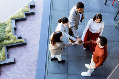 Five friends engage in an enthusiastic group handshake, showcasing their camaraderie and teamwork. The atmosphere is bright and lively, perfect for their outdoor meetup in the city.の写真素材