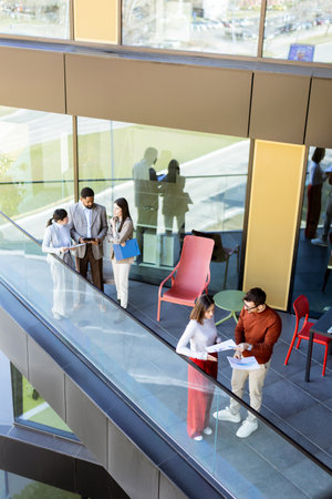 A group of professionals collaborates on a project while enjoying the airy space of a contemporary office balcony. Sunlight filters through large windows, enhancing their lively discussion.の写真素材