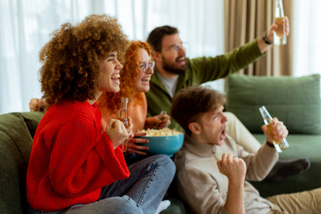 Laughter and excitement fill the air as friends gather in a warm living room, enjoying drinks and celebrating their favorite sports team during an exhilarating match.の写真素材
