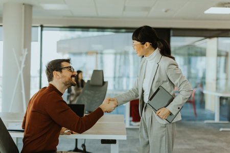 Two colleagues enjoy a moment of connection as they shake hands in a bright, contemporary office setting, signifying a successful collaboration and mutual respect.の写真素材
