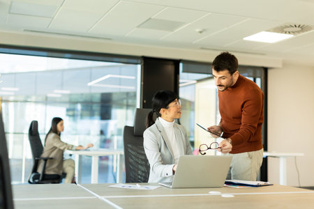 Colleagues discuss a project in a bright, contemporary office space. One partner gestures enthusiastically, while the other takes notes, showcasing teamwork and collaboration.の写真素材