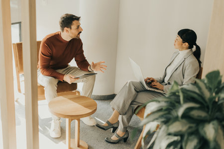 Two professionals engage in a thoughtful discussion in a stylish office setting, exchanging ideas while seated comfortably in contemporary chairs.の写真素材