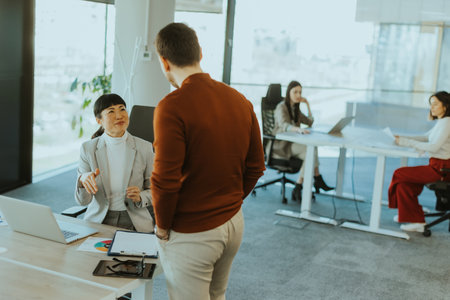 Two colleagues engage in a lively discussion in a contemporary office, exchanging ideas and insights while another team member works focused in the background.の写真素材