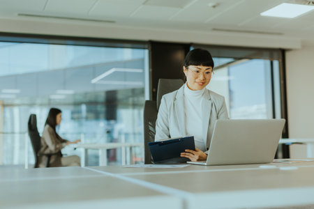 Asian businesswoman focus intently on  tasks in a chic office with large windows, creating a serene yet dynamic atmosphereの写真素材