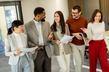 A group of professionals engages in lively discussions while reviewing documents, embodying teamwork and creativity in a bright, contemporary workspace filled with greenery.の写真素材