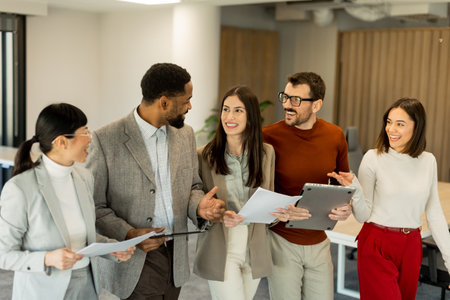A group of professionals engages in lively discussions while reviewing documents, embodying teamwork and creativity in a bright, contemporary workspace filled with greenery.の写真素材
