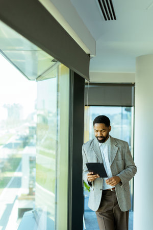 A well-dressed man reflects on his ideas while gazing through a large window in a contemporary office. Sunlight illuminates the space, creating a serene atmosphere for inspiration.の写真素材