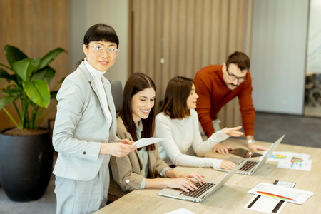 A diverse group of professionals engages in a dynamic brainstorming session. They exchange ideas, collaborate on laptops, and share documents in a bright, open workspace.の写真素材