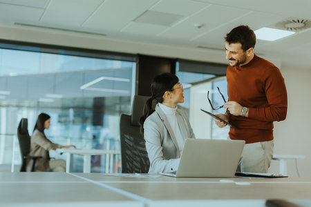 Two colleagues engage in a lively discussion in a contemporary office, exchanging ideas and insights while another team member works focused in the background.の写真素材