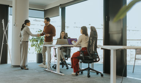 A group of four business professionals engages in a dynamic meeting at a contemporary office filled with natural light. Conversations flow as ideas are exchanged.の写真素材