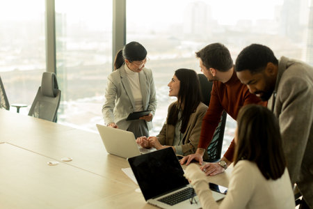 A diverse group of professionals collaborates around a table in a sleek office, sharing ideas and insights while utilizing laptops. The atmosphere is vibrant and engaging.の写真素材