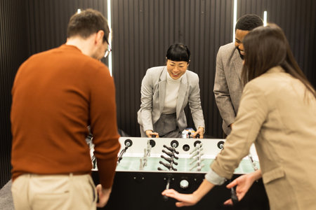 Friends gather around a sleek foosball table, their expressions filled with excitement and competition, enjoying an afternoon of fun in a stylish, contemporary setting.の写真素材