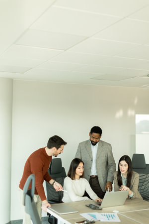 In a bright office, a diverse group of professionals gathers around a laptop, sharing insights and strategies while engaged in dynamic discussions, showcasing teamwork and creativity.の写真素材