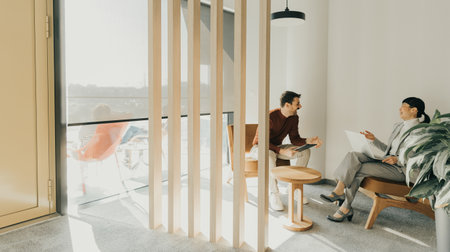 Two professionals engage in a thoughtful discussion in a stylish office setting, exchanging ideas while seated comfortably in contemporary chairs.の写真素材