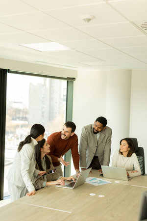 A diverse group of professionals collaborates around a table in a sleek office, sharing ideas and insights while utilizing laptops. The atmosphere is vibrant and engaging.の写真素材